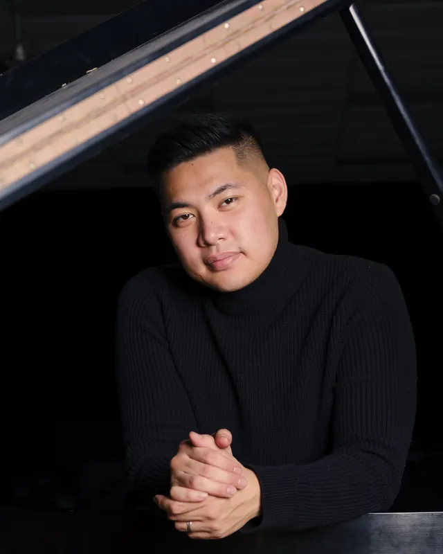 Isaac in a black turtleneck, hands clasped, smiling at the camera